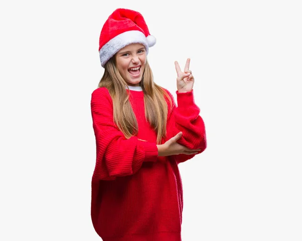 年轻美丽的女孩戴着圣诞节帽子在孤立的背景微笑与快乐的脸眨眼在相机做胜利标志 第二个 — 图库照片