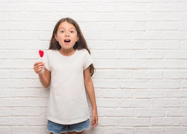 赤いハート キャンディー驚き顔 恐怖表現と興奮とショックで怖いを食べる白いレンガの壁にヒスパニック系の子供 — ストック写真