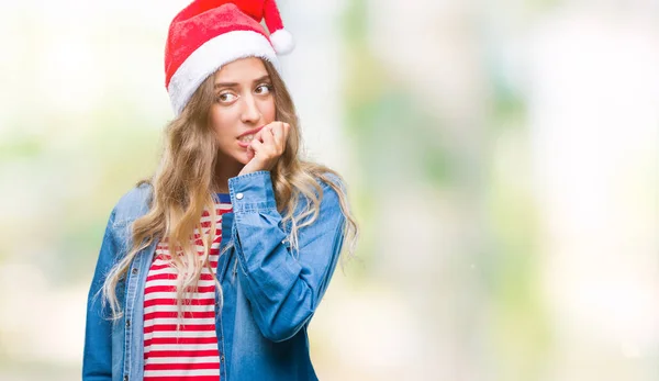 美しい若い金髪女性の不安や両手の爪を噛んで口の中で緊張を探して孤立の背景にクリスマス帽子をかぶっています 不安の問題 — ストック写真
