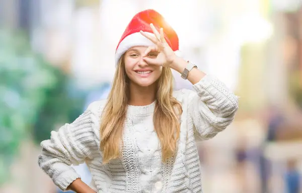 年轻美丽的金发女子戴着圣诞节帽子在孤立的背景做 手势与手微笑 眼睛看通过手指与幸福的脸 — 图库照片