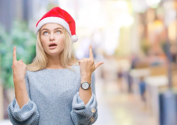 若い白人女性隔離された背景にクリスマスの帽子をかぶってびっくり驚いて見上げると指で指していると腕を上げた — ストック写真