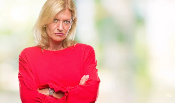 Middle age blonde woman over isolated background skeptic and nervous, disapproving expression on face with crossed arms. Negative person.