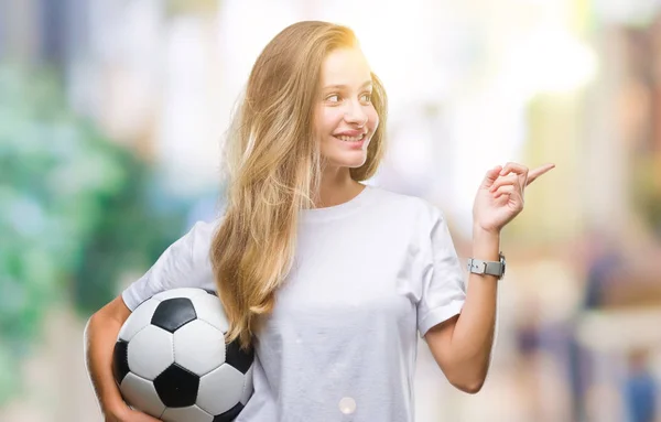 若い美しいブロンドの女性側の手と指で指す非常に幸せの孤立した背景にサッカー ボールを保持しています — ストック写真
