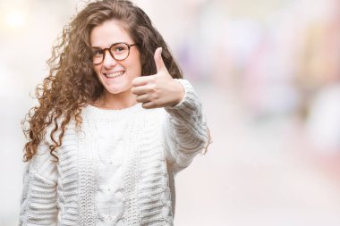 Güzel esmer kıvırcık saçlı Genç kız mutlu yaşasın el ile jest yapıyor izole arka plan üzerinde kış kazak giyiyor. Kameraya bakarak başarı gösteren ile ifade onaylama.