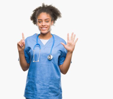 Genç afro Amerikalı doktor kadın gösterilen ve parmakları ile işaret izole arka plan yüzünden kendinden emin ve mutlu gülümseyerek süre 6 numara.