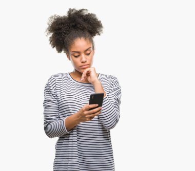 Genç afro Amerikalı kadın manifatura Smartphone izole arka plan ciddi bir yüz düşünme hakkında soru, çok karışık bir fikir üzerinde kullanma