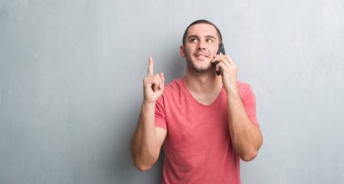 Gri grunge Genç beyaz adam bir fikirle sürpriz Evet duvar veya gülen yüz, bir numara ile işaret parmağı soru