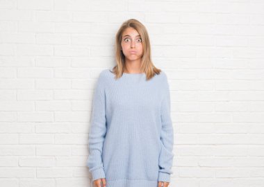 Komik surat ile yanakları şişirme beyaz tuğla duvarın üzerinden güzel ve genç birbayan. Ağız ile hava, deli ifade şişirilmiş.