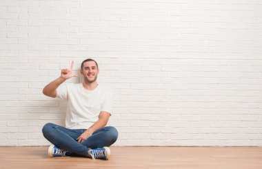 Gösterilen ve parmakları ile işaret beyaz tuğla duvarın üzerinden katta oturan genç beyaz adam ikincisi ise kendinden emin ve mutlu gülümseyerek.