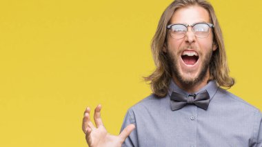 Genç yakışıklı adam uzun saçlı izole arka plan çılgın ve kızgın bağırarak ve agresif ifade ve silah kaldırdı bağırmaya papyon giyiyor. Hayal kırıklığı kavramı.