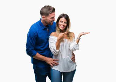 Hayret ve el ile sunulması ve parmak ile işaret ederken kameraya gülümseyen izole arka plan üzerinde aşık genç çift.