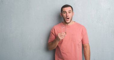 Bir bardak su şok sürpriz yüzü, korkuyor ve korku ifadesi ile heyecanlı olan korkmuş içme gri grunge duvarın üzerinden beyaz delikanlı