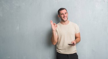Gri grunge üzerinde beyaz delikanlı duvar texting parmak, mükemmel sembolü ile ok işareti yapıyor smartphone kullanarak bir ileti