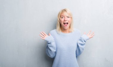 Grunge yetişkin beyaz kadın çılgın kutlama kış kazak giyen duvar gri ve çığlık kaldırdı ve açık gözleri heyecanlı silah ile başarı için hayrete düşürdü. Kazanan kavramı