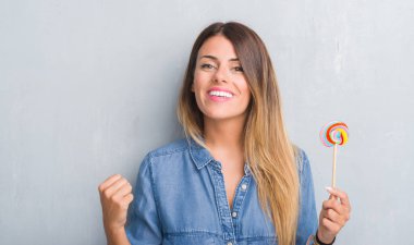 Duygu tezahürat Genç Yetişkin kadın gurur çığlık ve zafer ve başarı çok heyecanlı, kutluyor lolipop şeker yemek gri grunge duvarın üzerinden