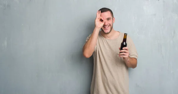 Jovem Caucasiano Homem Sobre Parede Grunge Cinza Segurando Cerveja Garrafa — Fotografia de Stock