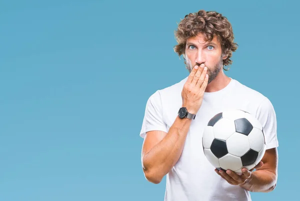 Handsome hispanic man model holding soccer football ball over isolated background cover mouth with hand shocked with shame for mistake, expression of fear, scared in silence, secret concept