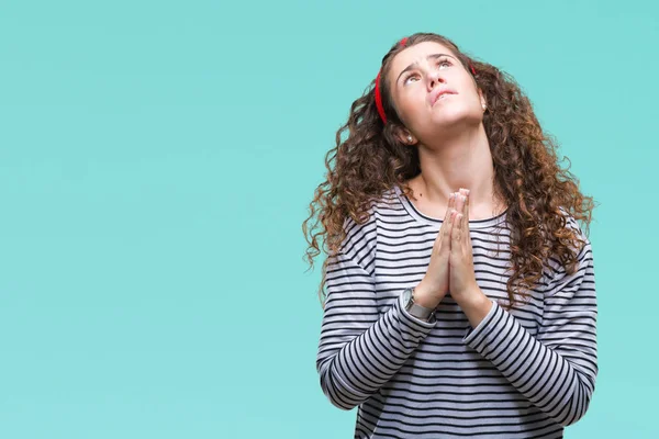 Beautiful brunette curly hair young girl wearing stripes sweater over isolated background begging and praying with hands together with hope expression on face very emotional and worried. Asking for forgiveness. Religion concept.