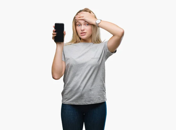 Young caucasian woman showing screen of smartphone over isolated background stressed with hand on head, shocked with shame and surprise face, angry and frustrated. Fear and upset for mistake.