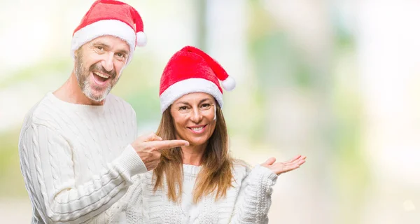 分離背景驚くし 手とを提示 指で指している間カメラに笑顔でクリスマスの帽子を着て中年ヒスパニック系カップル — ストック写真