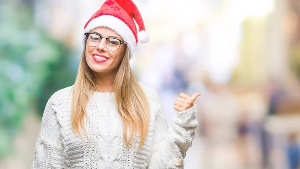 年轻美丽的妇女戴着圣诞节帽子在孤立的背景微笑与快乐的脸看和指向侧与拇指向上 — 图库照片