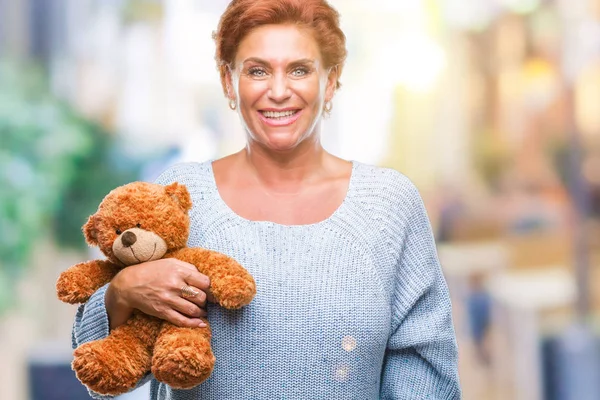 Senior caucasian woman holding teddy bear over isolated background with a happy face standing and smiling with a confident smile showing teeth