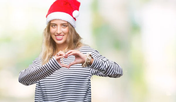 美しい若い金髪女性のハートマークと手で形を示す愛の笑みを浮かべて隔離された背景にクリスマス帽子をかぶっています ロマンチックな概念 — ストック写真