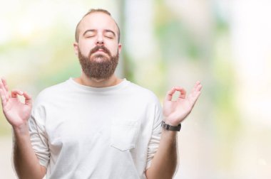 İzole arka plan üzerinde rahat t-shirt giyen genç beyaz hipster adam rahatla ve gülümseyen gözlerle kapalı parmak jestle meditasyon yapıyor. Yoga kavramı.