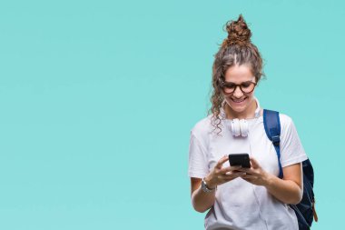 Sırt çantası, kulaklık ve smartphone izole arka plan üzerinde duran ve diş gösterilen kendine güvenen bir gülümsemeyle gülümseyerek mutlu bir yüz ile giyen genç esmer öğrenci kız