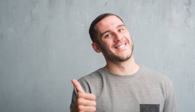 Ok işareti, başparmak ile parmak, mükemmel işareti yapıyor kocaman bir gülümseme ile mutlu gri grunge duvarın üzerinden beyaz delikanlı