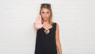 Güzel genç kadın ile güneş gözlüğü takmış beyaz tuğla duvarın üzerinden açık el dur işareti ile ciddi ve kendine güvenen ifade, savunma hareketi yapıyor