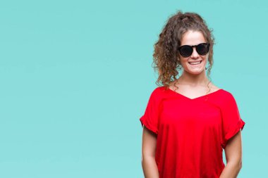 Güzel esmer kıvırcık saçlı Genç kız yüzünde mutlu ve güzel bir gülümseme ile izole arka plan üzerinde güneş gözlüğü takıyor. Şanslı kişi.