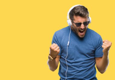 Üzerinden müzik kulaklık giyen genç yakışıklı adam arka plan çok mutlu ve heyecanlı kaldırdı, silah ile kazanan jest yapıyor gülümseyen ve başarı için çığlık izole. Kutlama kavramı.