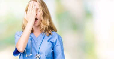 Üzerinde tıbbi üniforma giyen güzel genç doktor kadın yarım yüz, göz ve ağız el ile kapsayan Yawning yorgun arka plan izole. Acı yüzü acıyor.