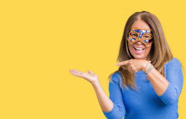 Hayret ve el ile sunulması ve parmak ile işaret ederken kameraya gülümseyen izole arka plan üzerinde Venedik karnaval maskesi giyen güzel orta yaş kadın.