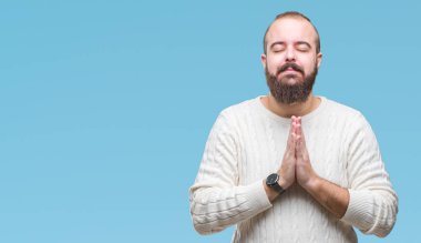 Ellerle birlikte AF emin gülümseyen için soran dua izole arka plan üzerinde kış kazak giyen genç beyaz hipster adam.