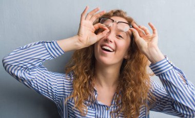 Gri grunge Duvar ile mutlu yüz el parmaklarının arasından seyir göz üzerinde ok işaretiyle yapıyor gülümseyen genç Kızıl saçlı kadın