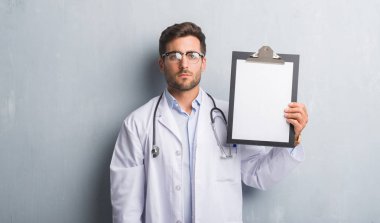 Yakışıklı genç doktor adam Pano acımak yüz ciddi düşünüyorum üstünde kendine güvenen bir ifade ile tutarak gri grunge duvarın üzerinden