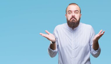 Genç beyaz hipster adam izole arka plan clueless ve şaşkın bir ifadeyle kollar ve eller kaldırdı. Şüphe kavramı.