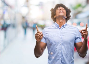 Afro Amerikalı adam izole arka plan üzerinden hayran ve yukarıya bakıp parmakları ile işaret şaşırttı ve silah kaldırdı.