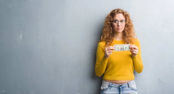 Joven Pelirroja Sobre Gris Pared Grunge Sosteniendo Dólar Con Una — Foto de Stock