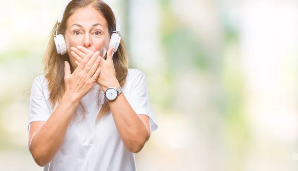 中年西班牙妇女听音乐戴耳机在孤立的背景震惊覆盖嘴与手的错误 秘密概念 — 图库照片