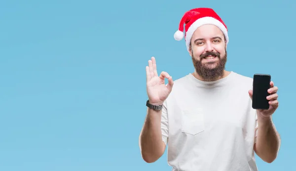 Junge Kaukasische Mann Mit Weihnachtsmütze Zeigt Smartphone Bildschirm Über Isoliertem — Stockfoto