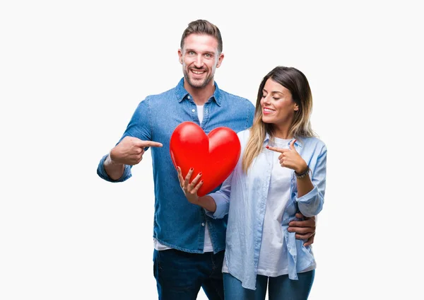 年轻夫妇在爱持有红色心脏在孤立的背景非常高兴地指着手和手指 — 图库照片
