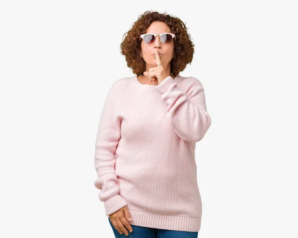 美しい中間エイガー年配の女性の唇に指で静かにするように求めて孤立の背景にピンクのセーター サングラスを着用します 沈黙と秘密の概念 — ストック写真