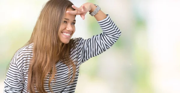 上のストライプのセーターを着ている若い美しいブルネットの女性は 非常に幸せと笑顔の頭上の手で遠く離れている背景を分離しました 概念を検索 — ストック写真