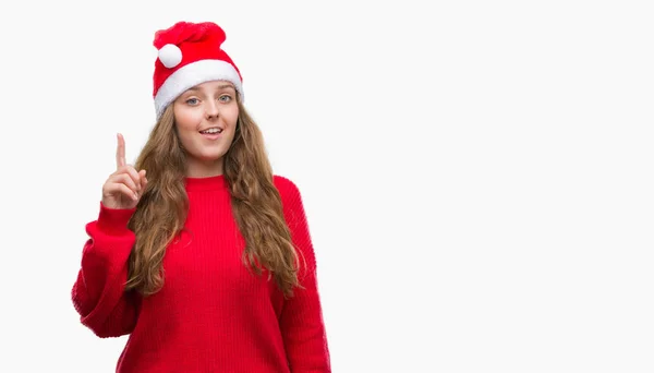 年轻的金发碧眼的女人戴着圣诞老人的帽子惊讶的想法或问题用快乐的脸指指点点 — 图库照片