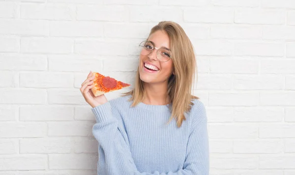 美丽的年轻女子在白色砖墙吃比萨饼片与幸福的脸站着 面带微笑 自信的微笑显示牙齿 — 图库照片