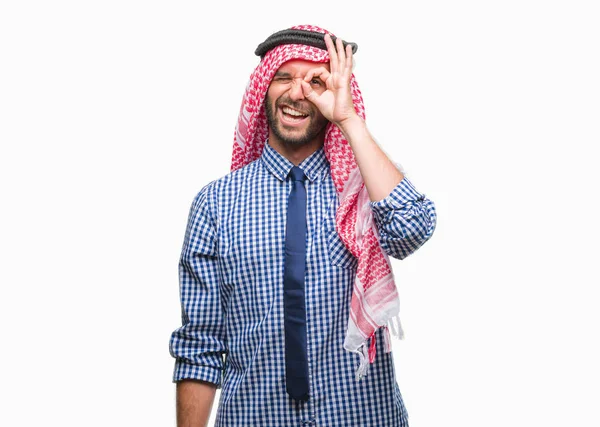 年轻英俊的阿拉伯商人穿着 Keffiyeh 在孤立的背景下做 手势用手微笑 眼睛看通过手指与愉快的面孔 — 图库照片