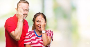 Orta yaş İspanyol çift el yüz ve sürpriz duygu kendinden emin gülümseme ile tek gözüyle kapsayan izole arka plan üzerinde aşık.